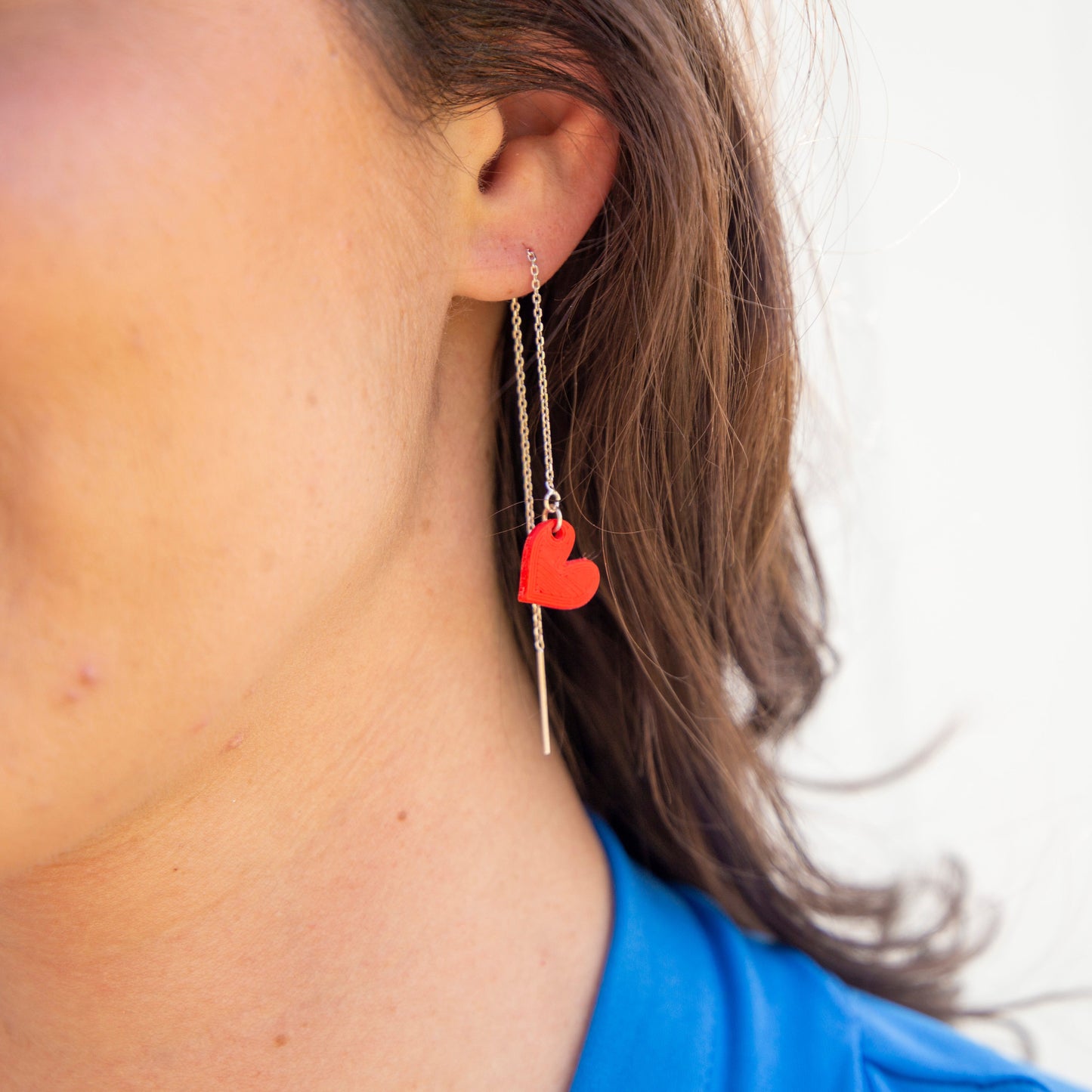 Close-up of a person wearing a red heart-shaped earring with a white background