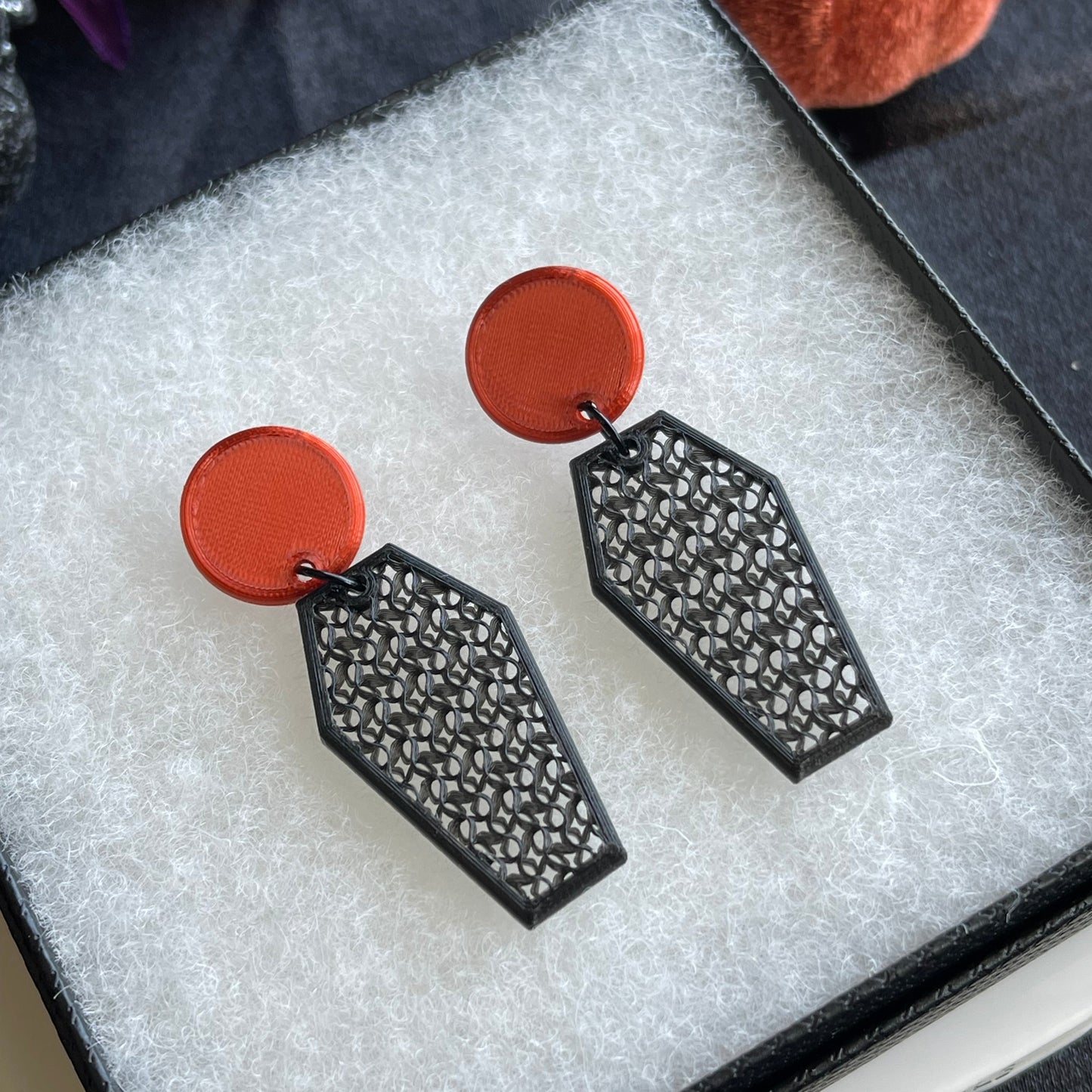 Pair of earrings with burnt orange circular ends and black geometric designs on a textured surface.