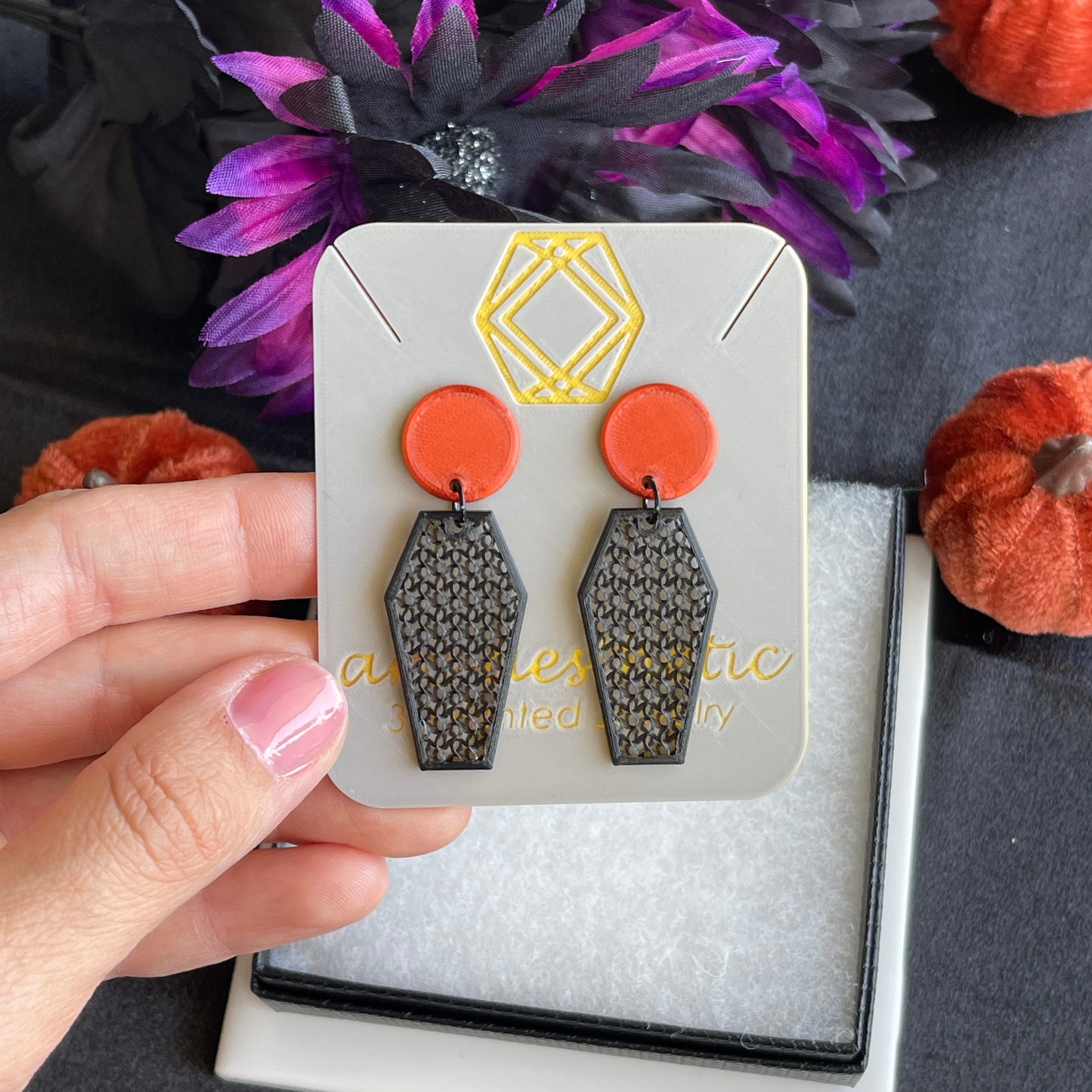 Hand holding a card with earrings against a dark background with decorative elements.