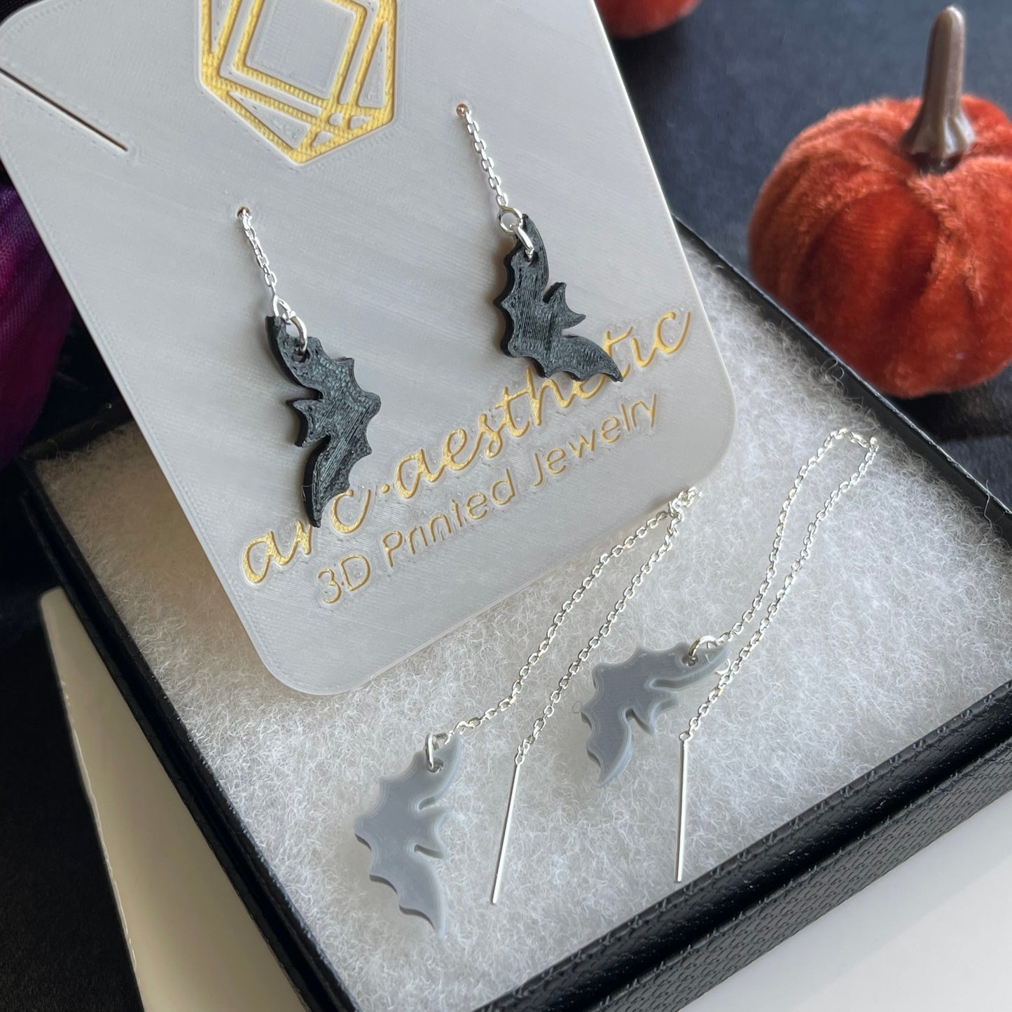 Silver bat-shaped jewelry set on a branded card with pumpkins in the background