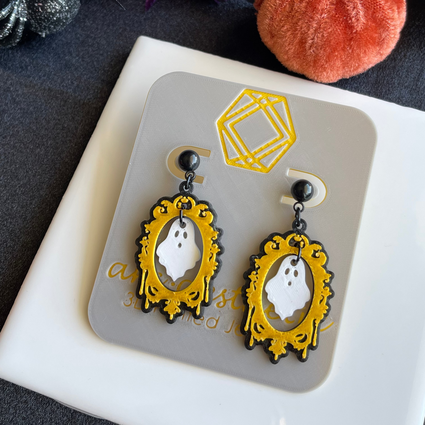 Ghost-themed earrings on a display card with Halloween decorations in the background.