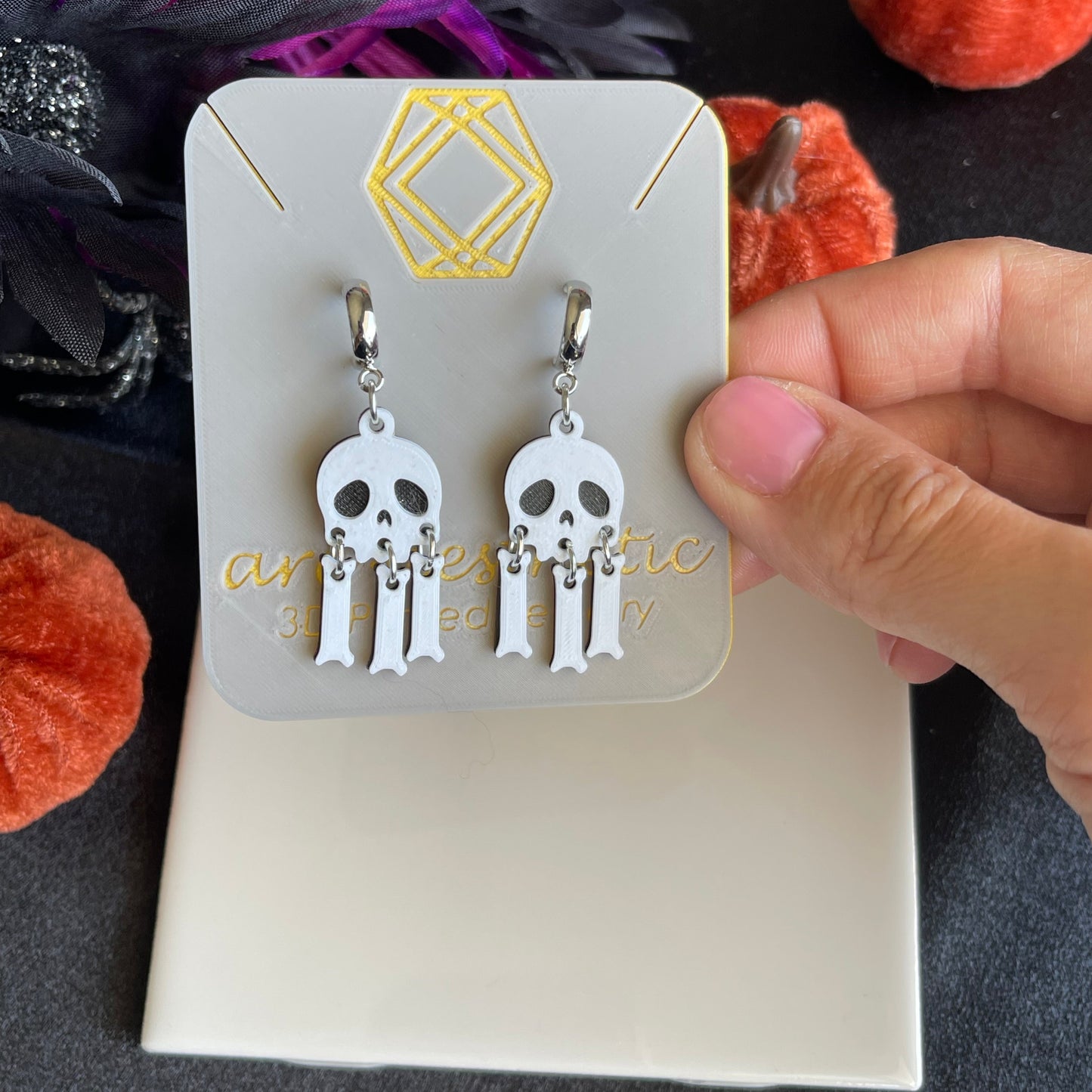 Pair of skull-shaped earrings on a card with decorative elements in the background