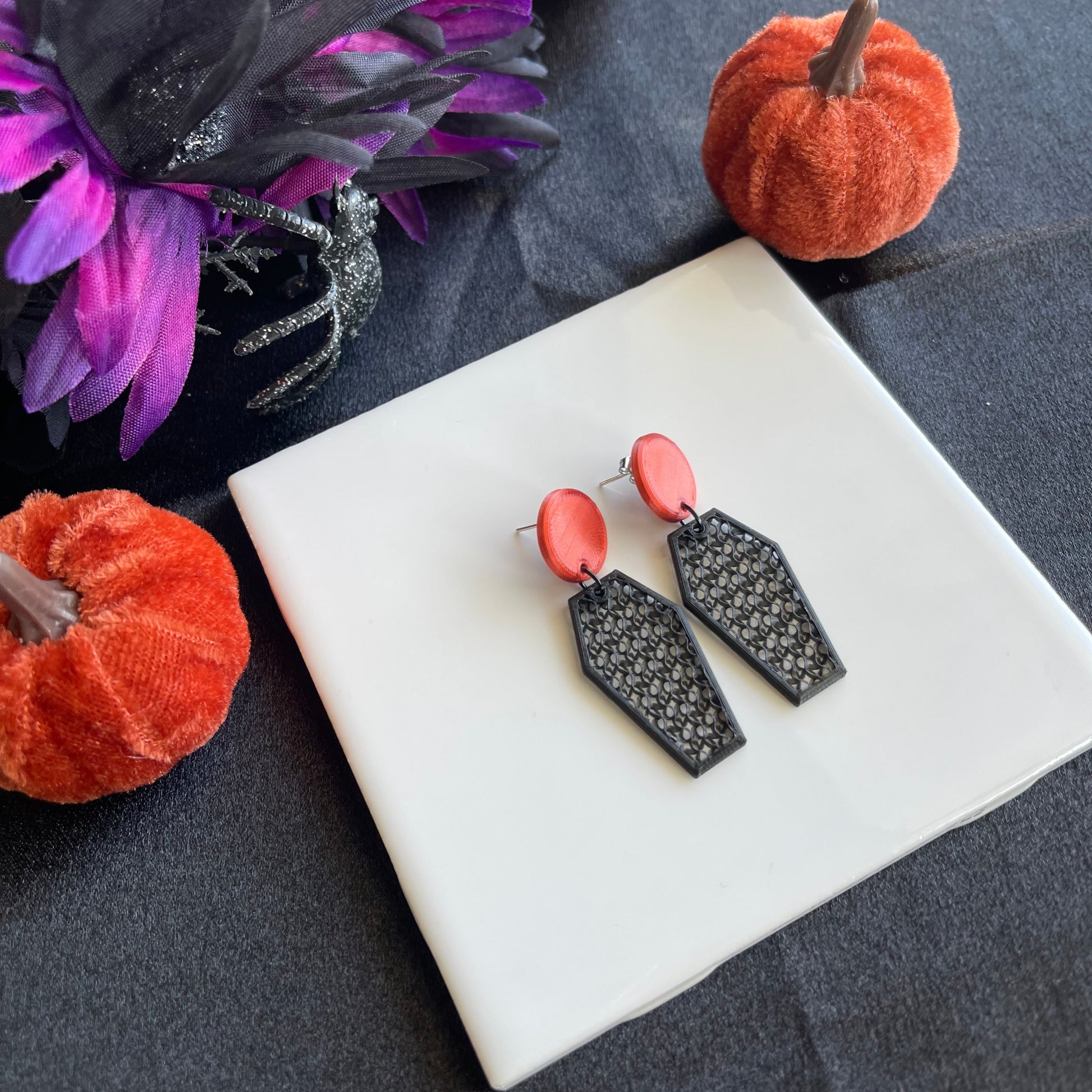 Black and burnt orange earrings on a white square platform with Halloween-themed decorations.