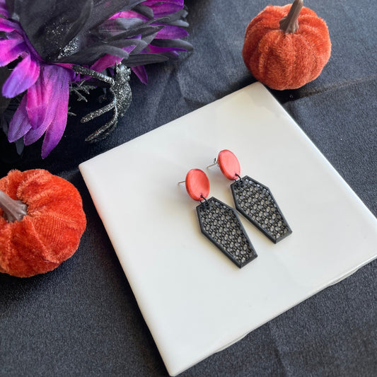 Black and burnt orange earrings on a white square platform with Halloween-themed decorations.