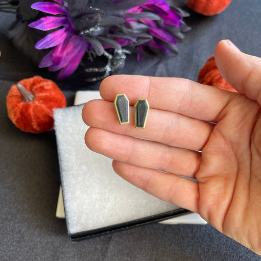Hand holding two small geometric earrings with Halloween decorations in the background