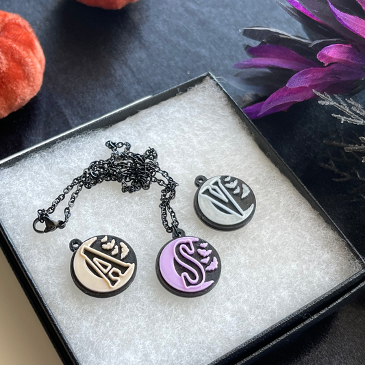 Necklace with four round pendants in a box on a dark surface with purple flowers